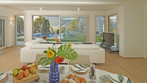 A modern hotel room with a large bed, a dining table with breakfast items, a vase with flowers, and a city view through large windows. - Villa Bianca (San Felice del Benaco)