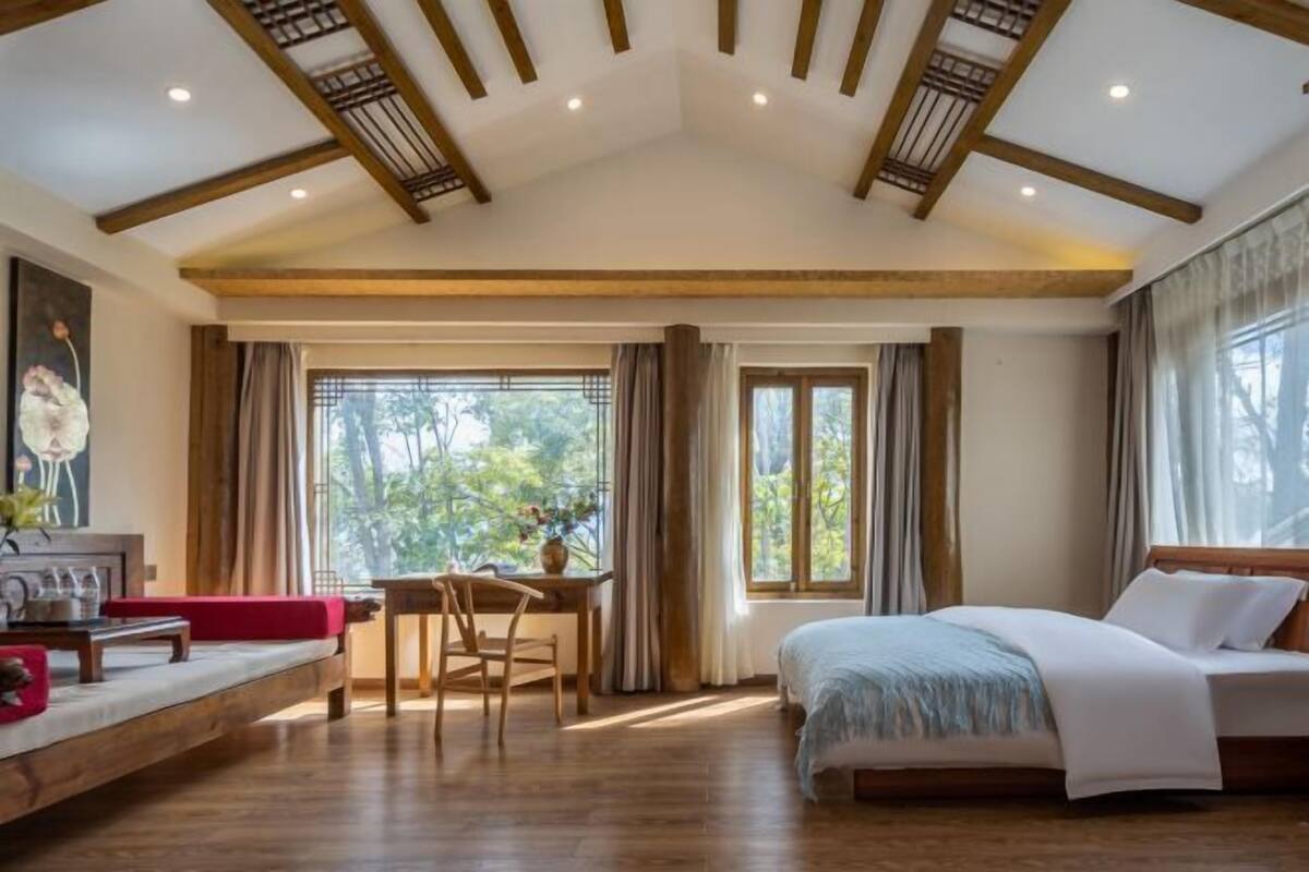Un dormitorio amplio con una cama grande, un escritorio de madera y una zona de estar con un sofá rojo.