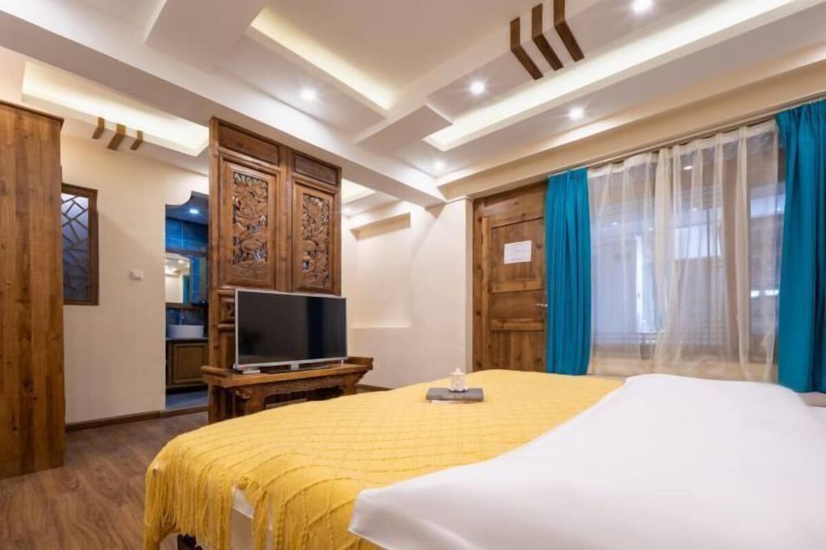 Habitación de hotel con cama, televisión, detalles de madera y vistas al exterior.