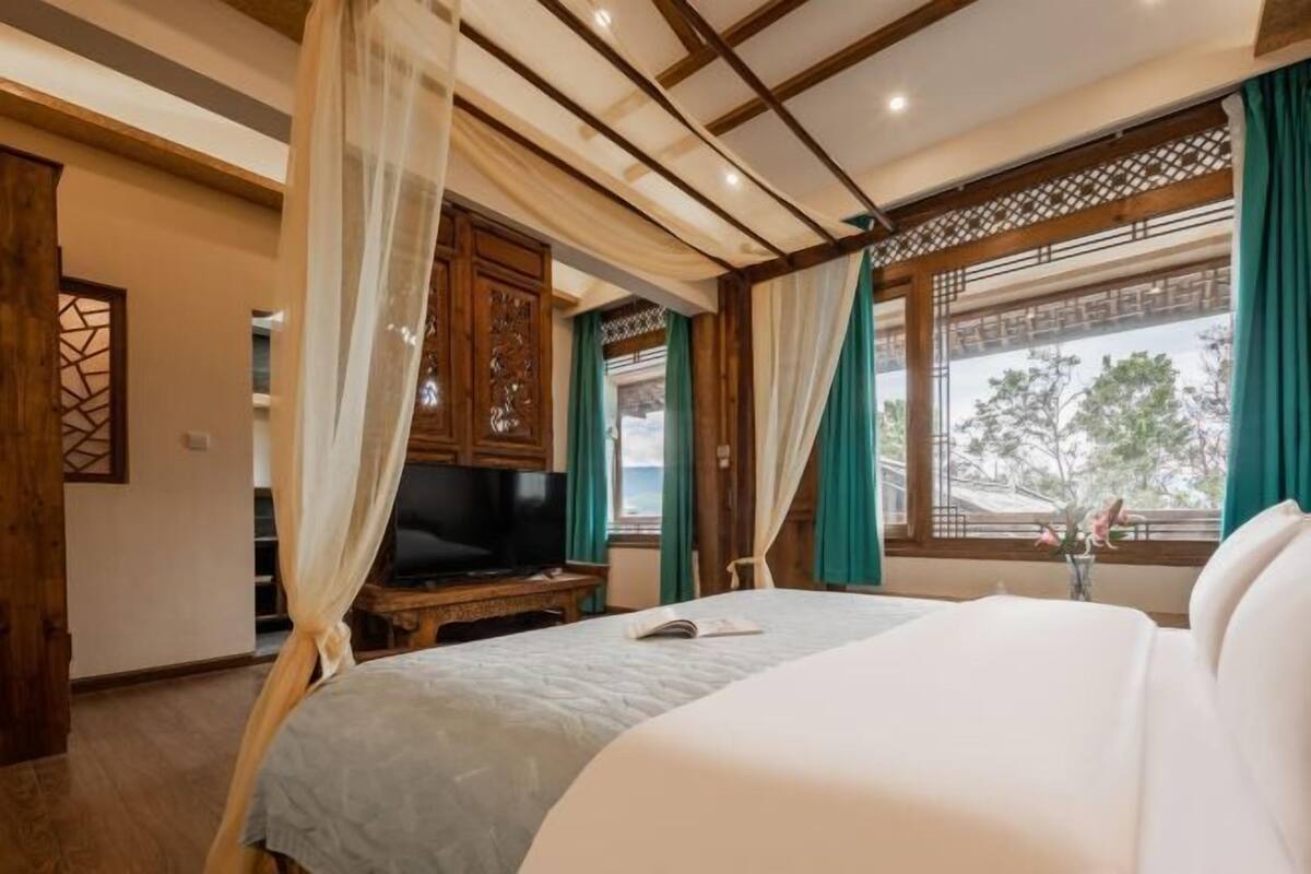 Un dormitorio con cama, televisor y ventana con cortinas.
