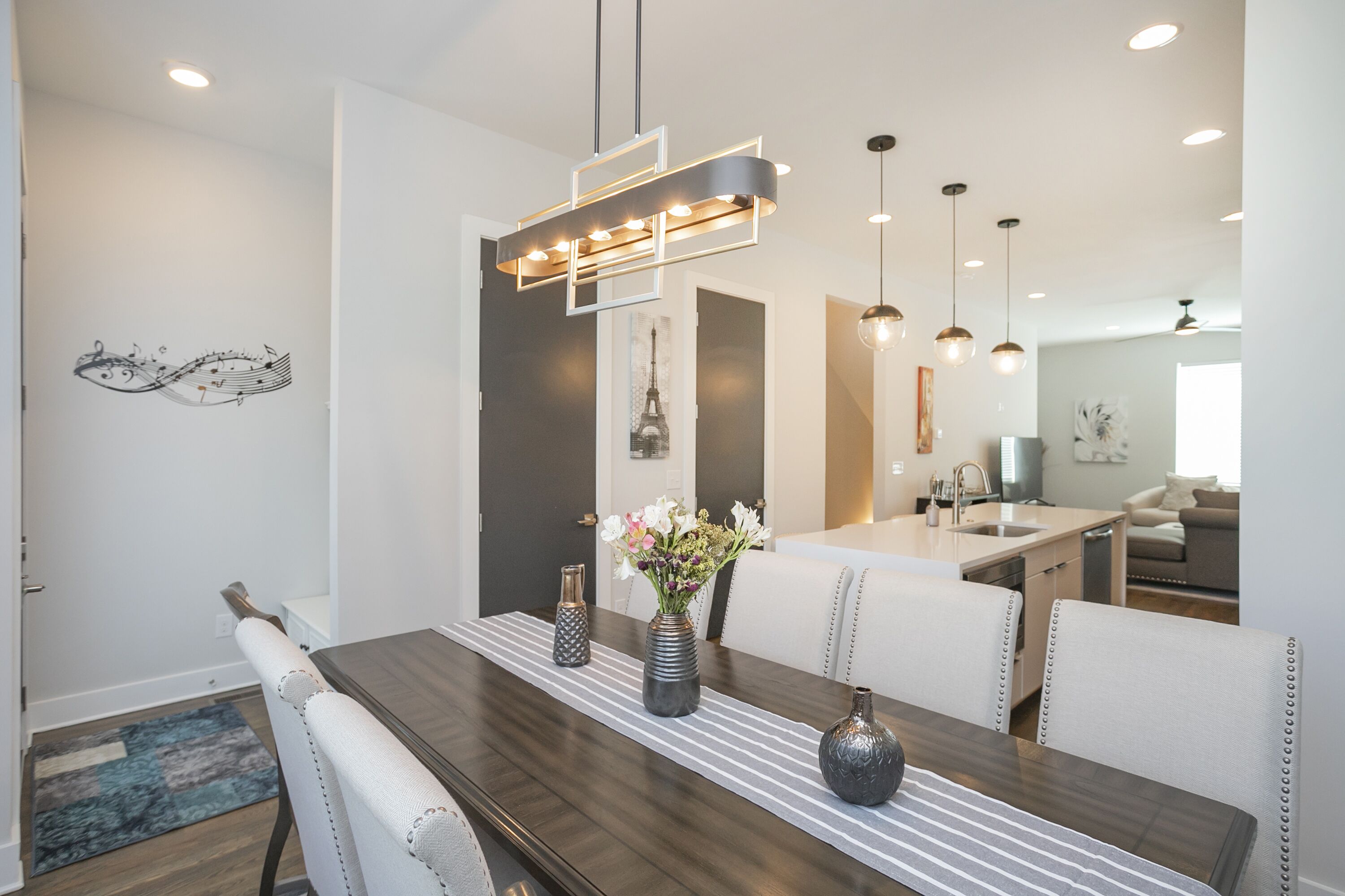 Un comedor moderno con una mesa de madera, sillas blancas tapizadas y una lámpara colgante contemporánea.