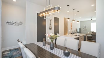 Un comedor moderno con una mesa de madera, sillas blancas tapizadas y una lámpara colgante contemporánea.