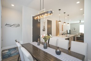 A modern dining area with a wooden table, white upholstered chairs, and a contemporary pendant light.