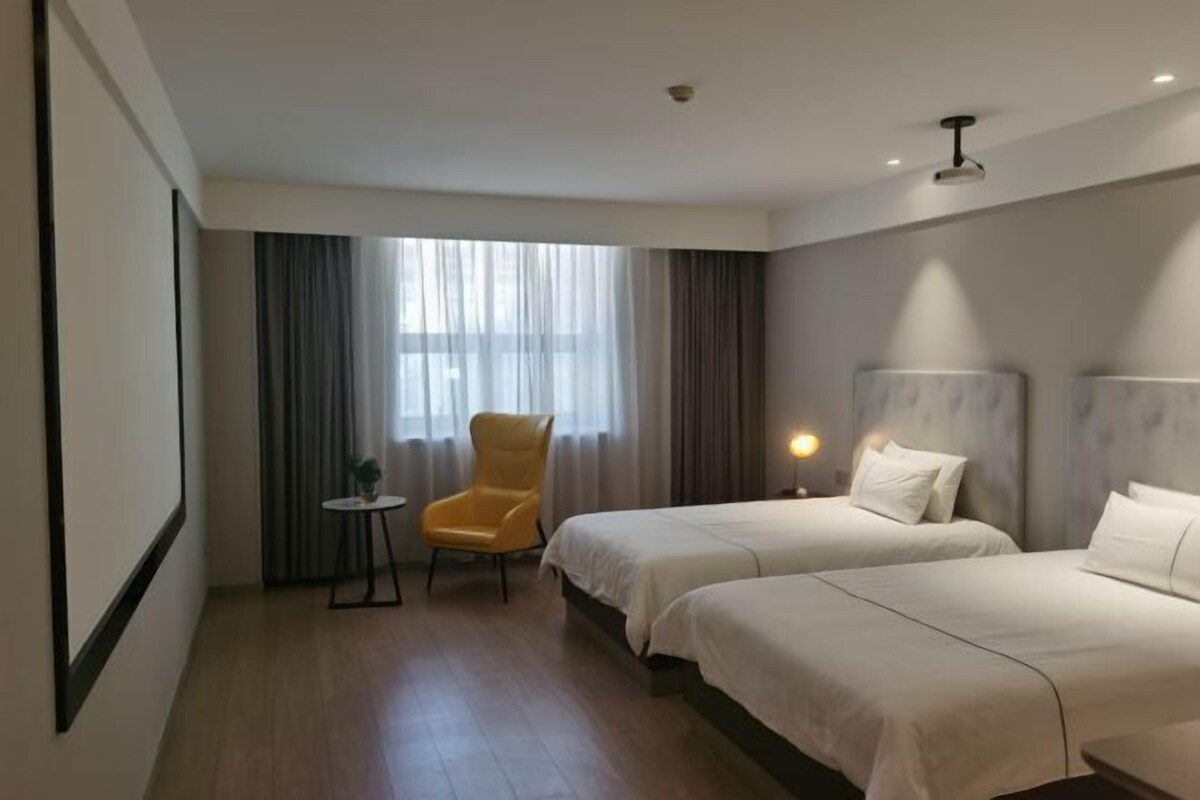 Une chambre d’hôtel avec deux lits, une chaise, une petite table et une fenêtre avec des rideaux.