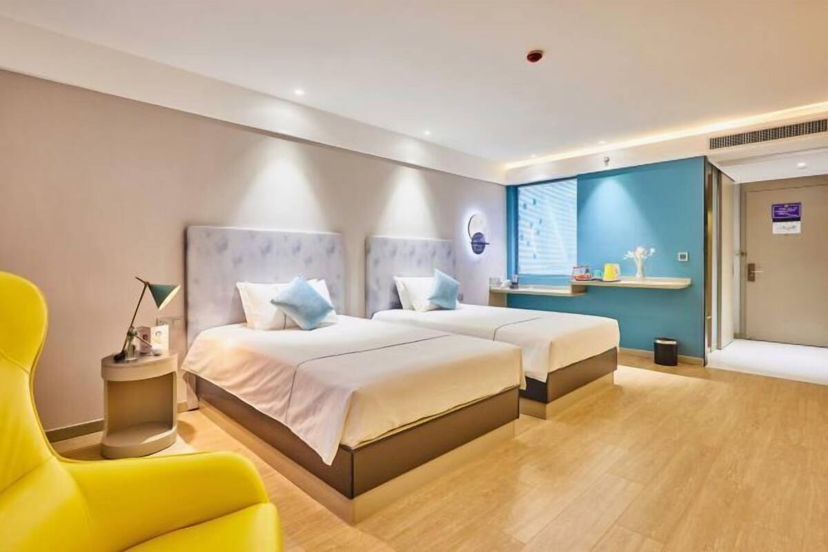 Ein Hotelzimmer mit zwei Betten, einem kleinen Schreibtisch, einem Stuhl und einer Badezimmertür.