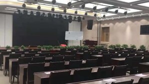 A conference room with rows of tables and chairs, a stage with a black backdrop, and a whiteboard. - Magnotel Hotel (Weinan Duhua Road Haixing City) (Weinan)