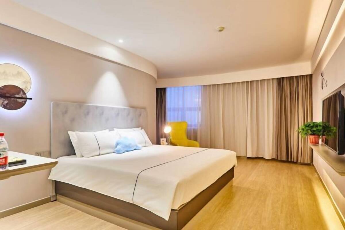 Ein modernes Hotelzimmer mit Bett, Nachttisch, Lampe, Vorhängen und Fernseher.