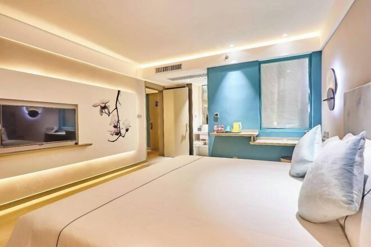 Ein modernes Hotelzimmer mit einem großen Bett, einem an der Wand montierten Fernseher und einem Fenster mit Jalousien.