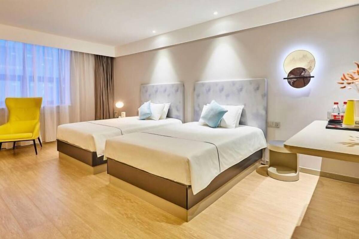 Ein Hotelzimmer mit zwei Betten, einem gelben Sessel, einem Nachttisch und einer Wandleuchte.