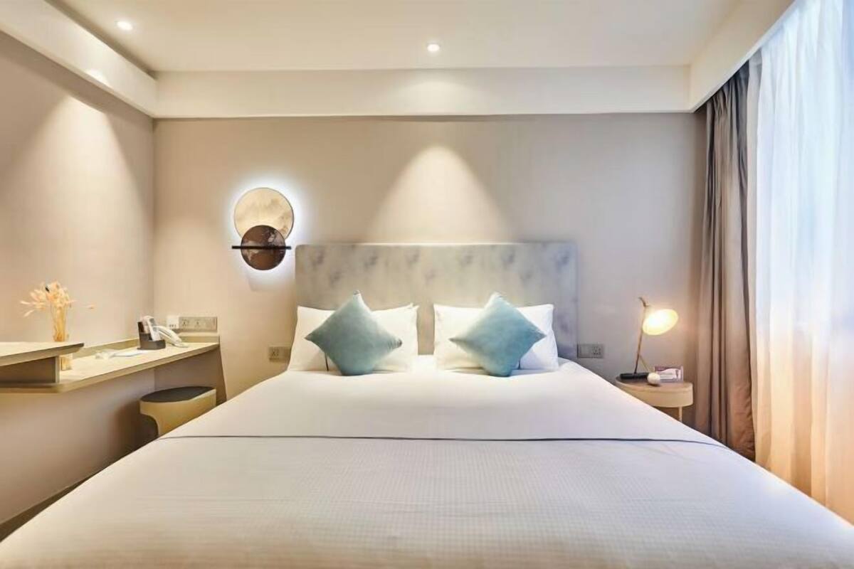 Ein Hotelzimmer mit einem großen Bett, einem Nachttisch, einer Wandleuchte und einem kleinen runden Spiegel.