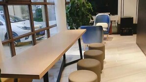A modern interior with a wooden table and four beige stools, a blue chair, and a large potted plant. - Magnotel Hotel (Weinan Duhua Road Haixing City) (Weinan)