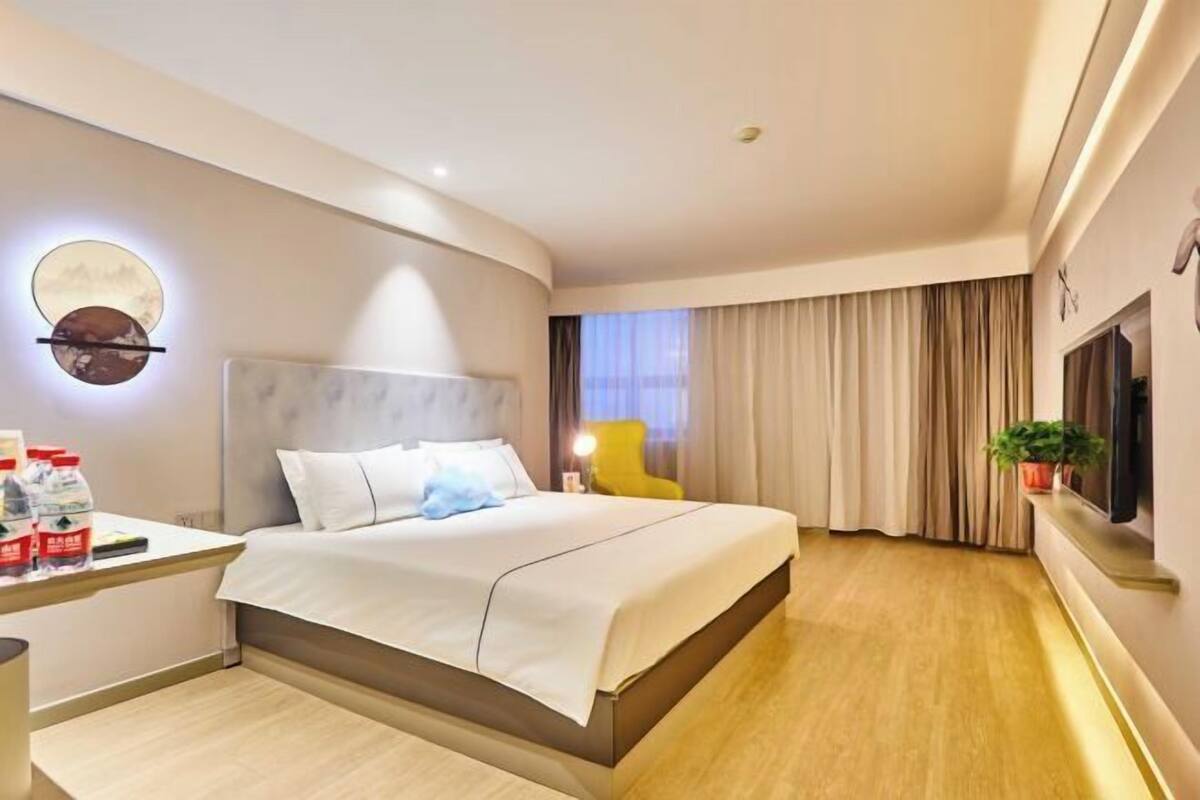 Ein modernes Hotelzimmer mit Bett, Nachttisch, Lampe und einem am Wand montierten Fernseher.