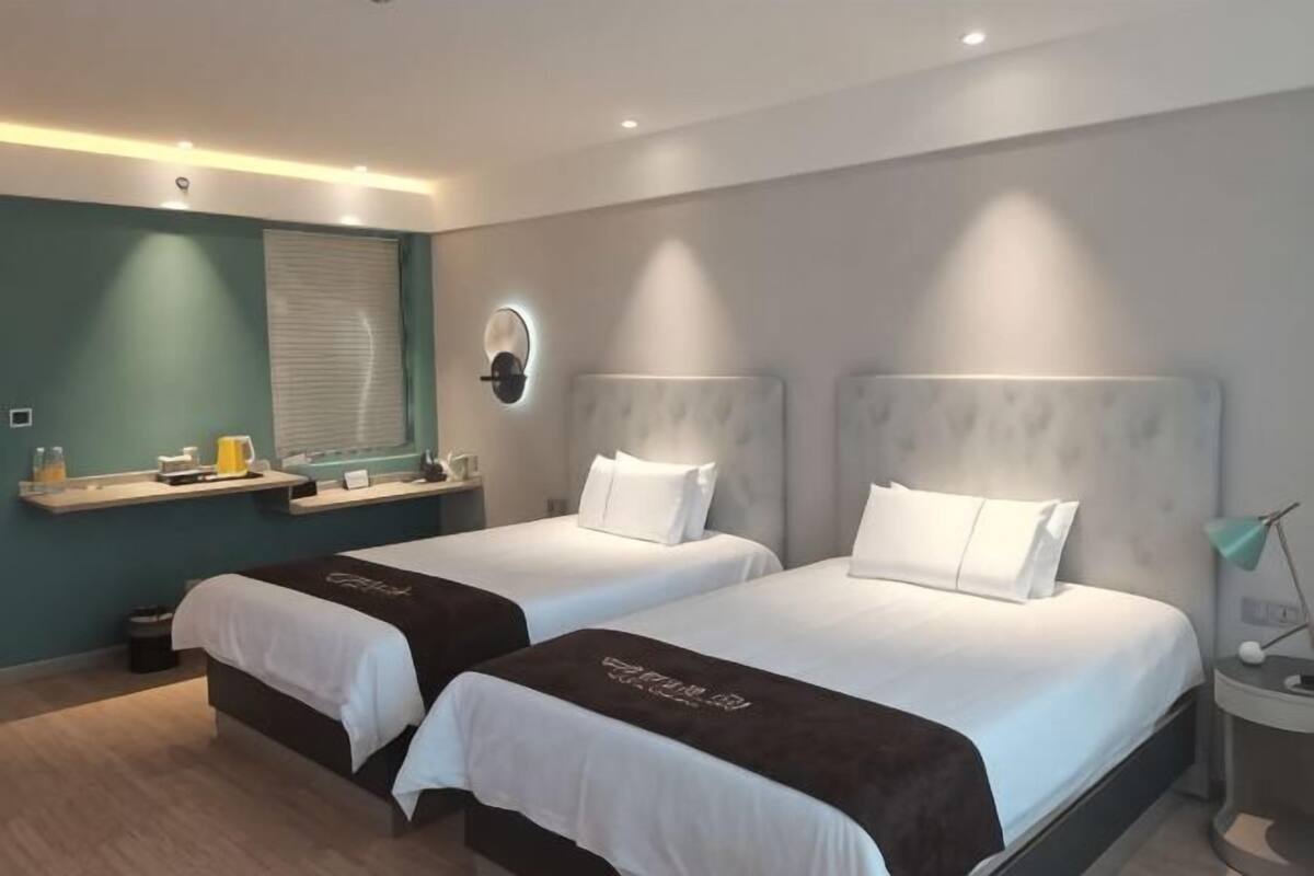 Ein Hotelzimmer mit zwei Betten, einem kleinen Schreibtisch, einem Spiegel und einem Fenster mit Jalousien.