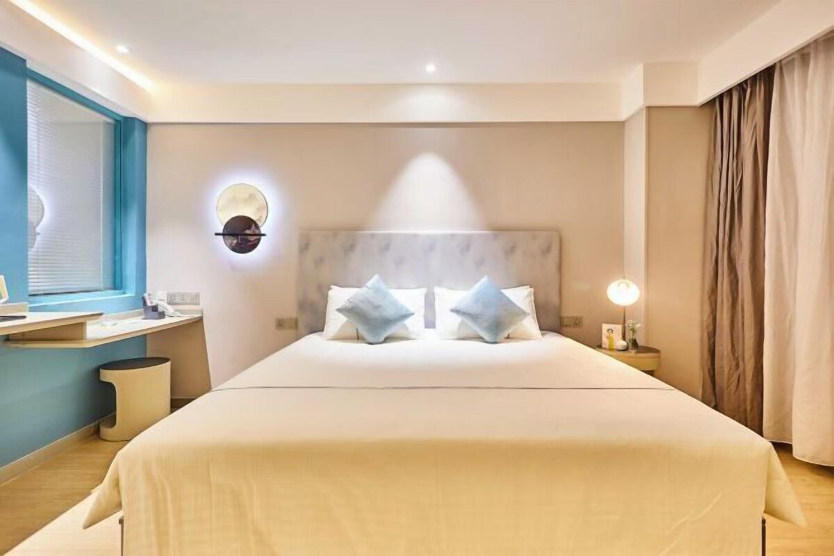 Une chambre d’hôtel comprenant un lit, une table de chevet, une lampe et un luminaire circulaire fixé au mur.