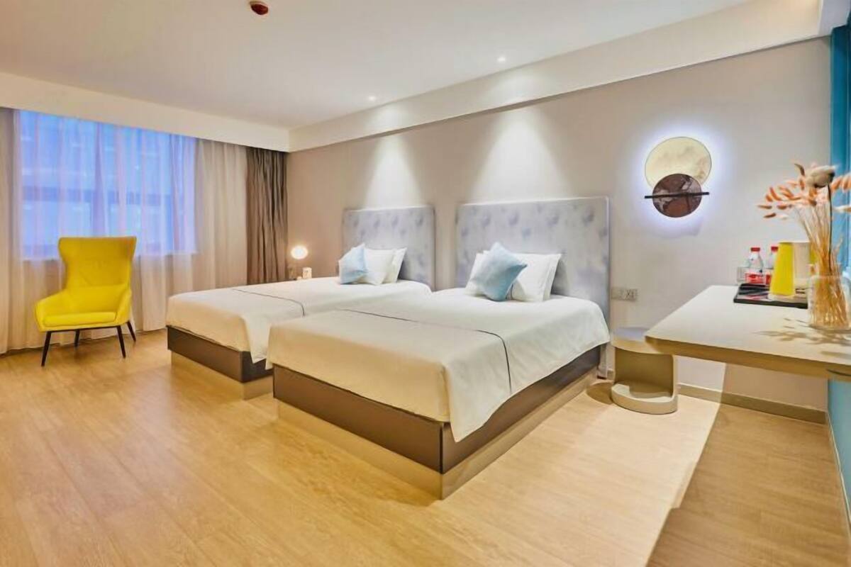 Ein Hotelzimmer mit zwei Betten, einem Schreibtisch, einem Stuhl und einem großen Fenster mit Vorhängen.