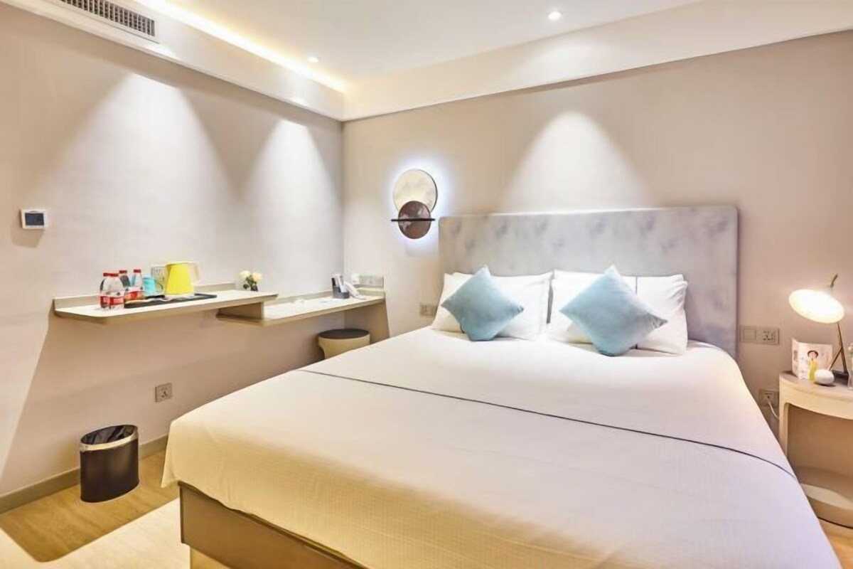 Une chambre d’hôtel avec un grand lit, des tables de chevet, une lampe fixée au mur et une petite poubelle.