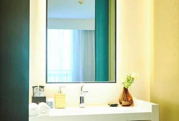 Une salle de bain avec un lavabo blanc, un miroir et un vase rempli de fleurs.