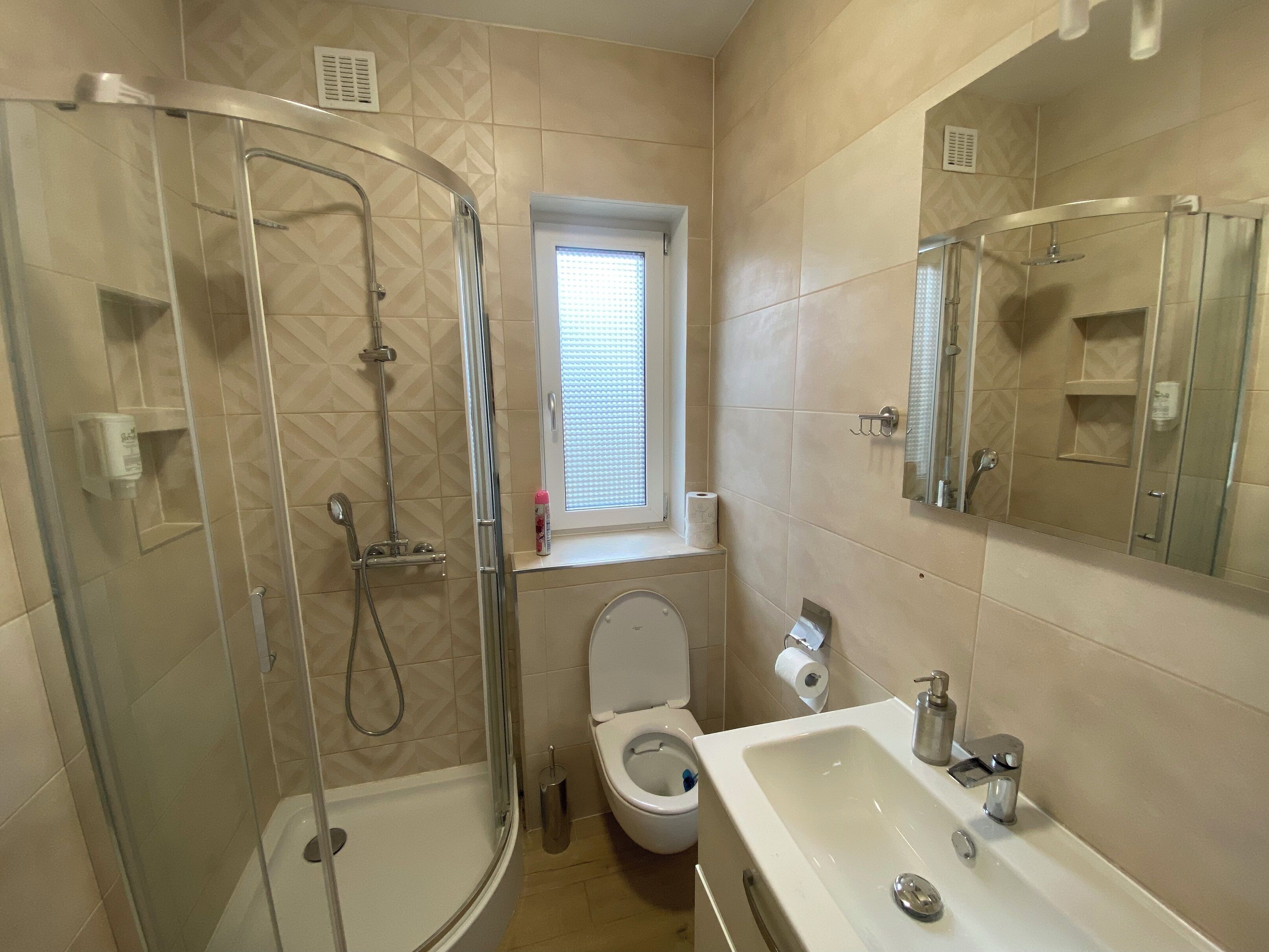 A bathroom with a glass-enclosed shower, a toilet, a sink, and a window.