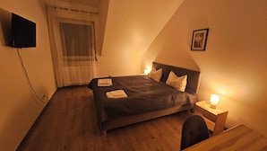A bedroom with a bed, bedside tables, a desk, a chair, a TV, and a window with curtains. - Diamentowa 7 Rent Home (gmina Dopiewo)