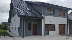A two-story house with a grey roof, a small window on the first floor, and a number '7' on the wall. - Diamentowa 7 Rent Home (gmina Dopiewo)