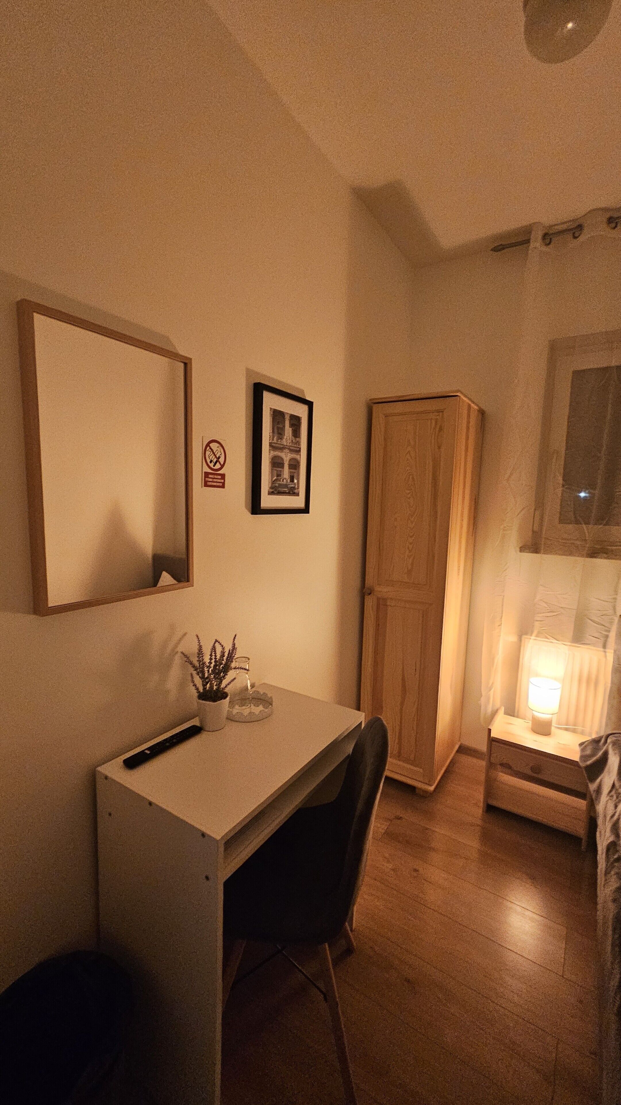 A room with a desk, chair, wardrobe, and a bed with a nightstand.