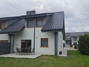 A two-story residential building with a tiled roof, a balcony, and a patio with outdoor furniture. - Diamentowa 7 Rent Home (gmina Dopiewo)
