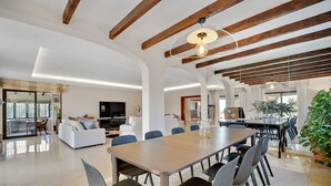 A spacious living area with a wooden ceiling, a dining table with chairs, and a large plant. - Villa Xula - Marbella Club (Marbella)