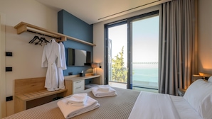 Ett hotellrum med en säng, ett nattduksbord i trä, en tv, en klädställning och utsikt över havet.