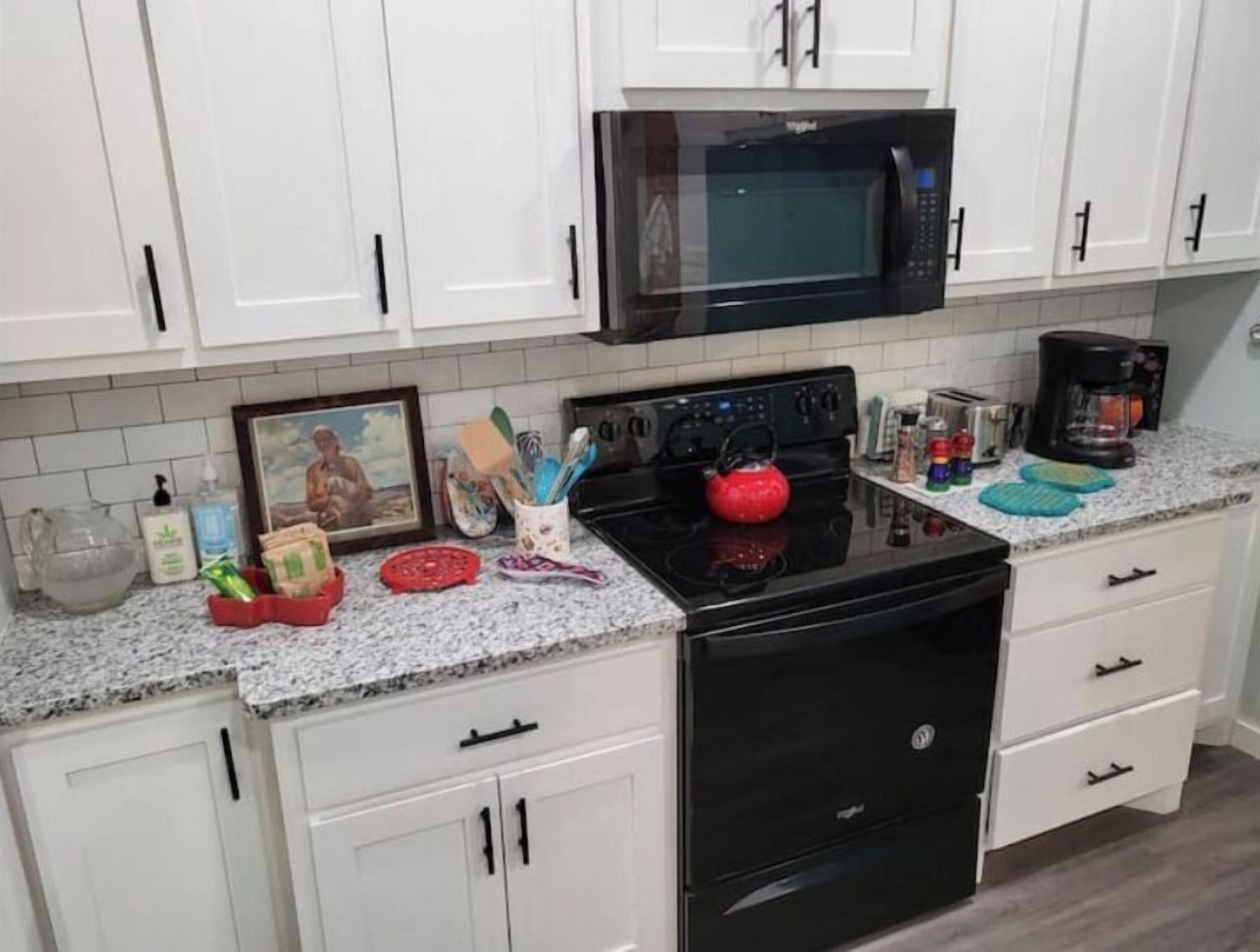 A kitchen with white cabinets, a black microwave, a red kettle, and various kitchen items on the countertop.