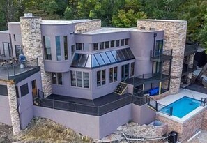 Una casa moderna de varios pisos con piscina, pilares de piedra y ventanas amplias.