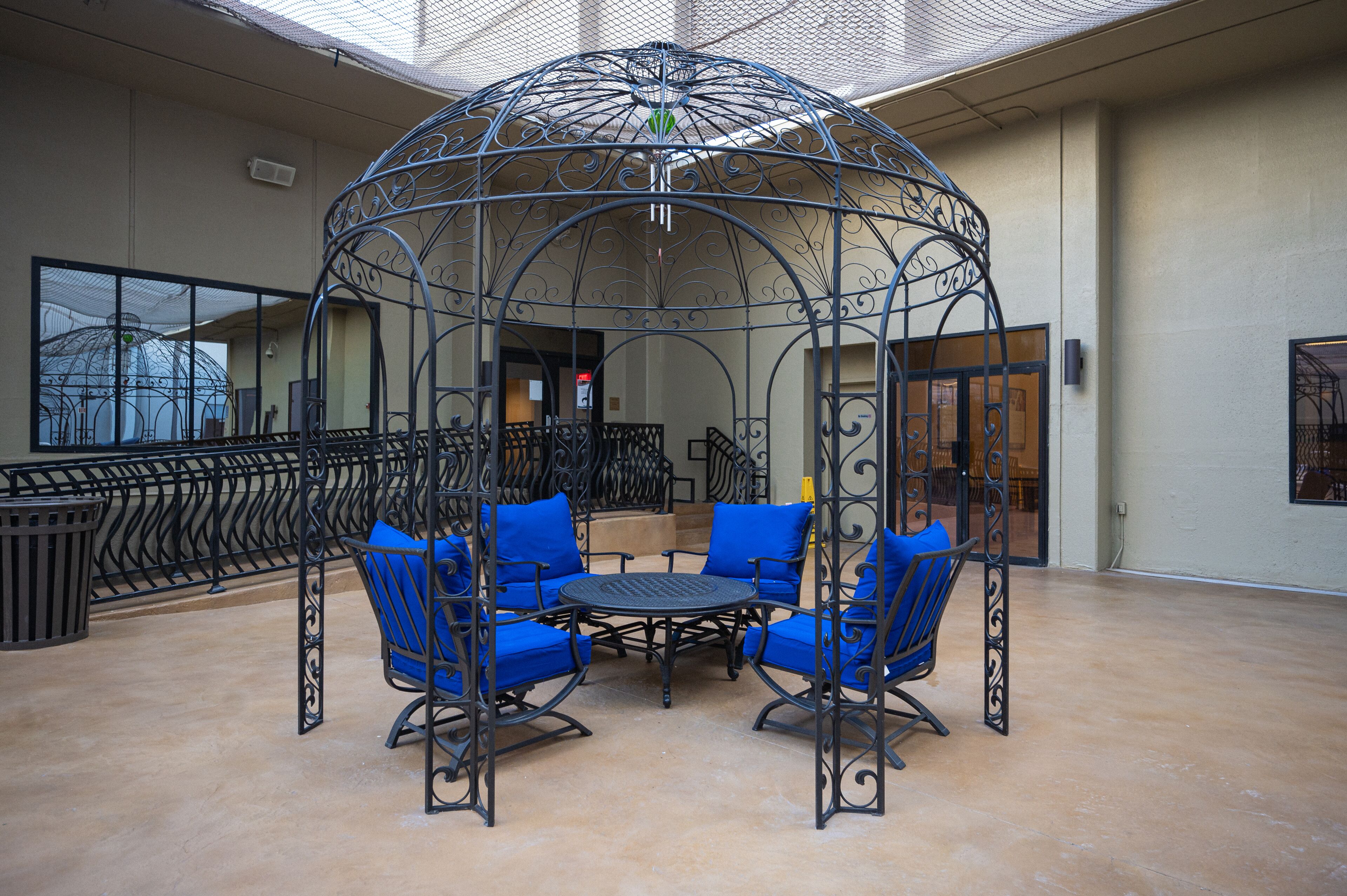 Un espace extérieur aménagé avec des sièges, abrité par un gazebo en fer forgé, des chaises rembourrées bleues et une table ronde.