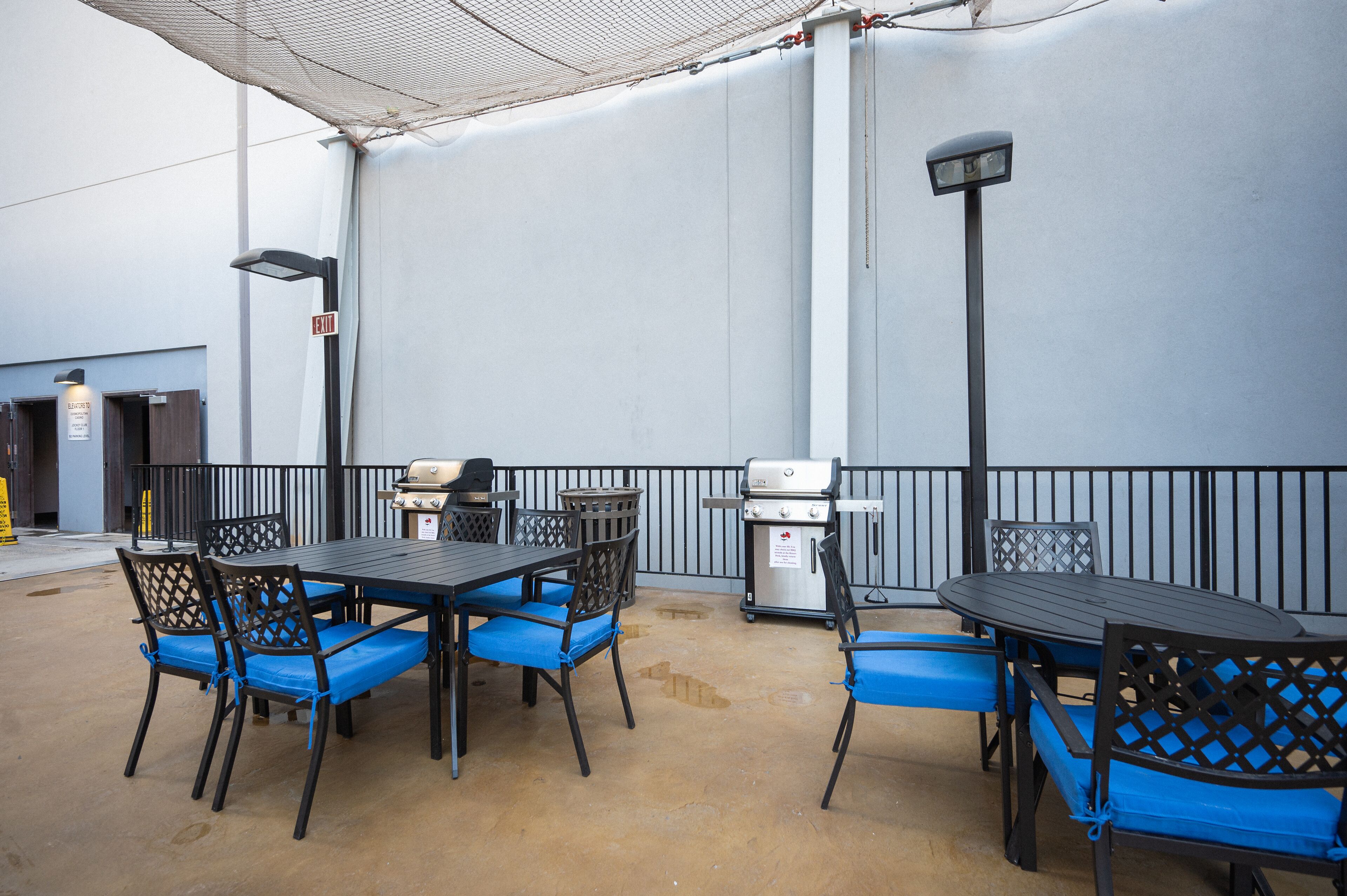 An outdoor patio area with tables and chairs, a grill, and a trash can.