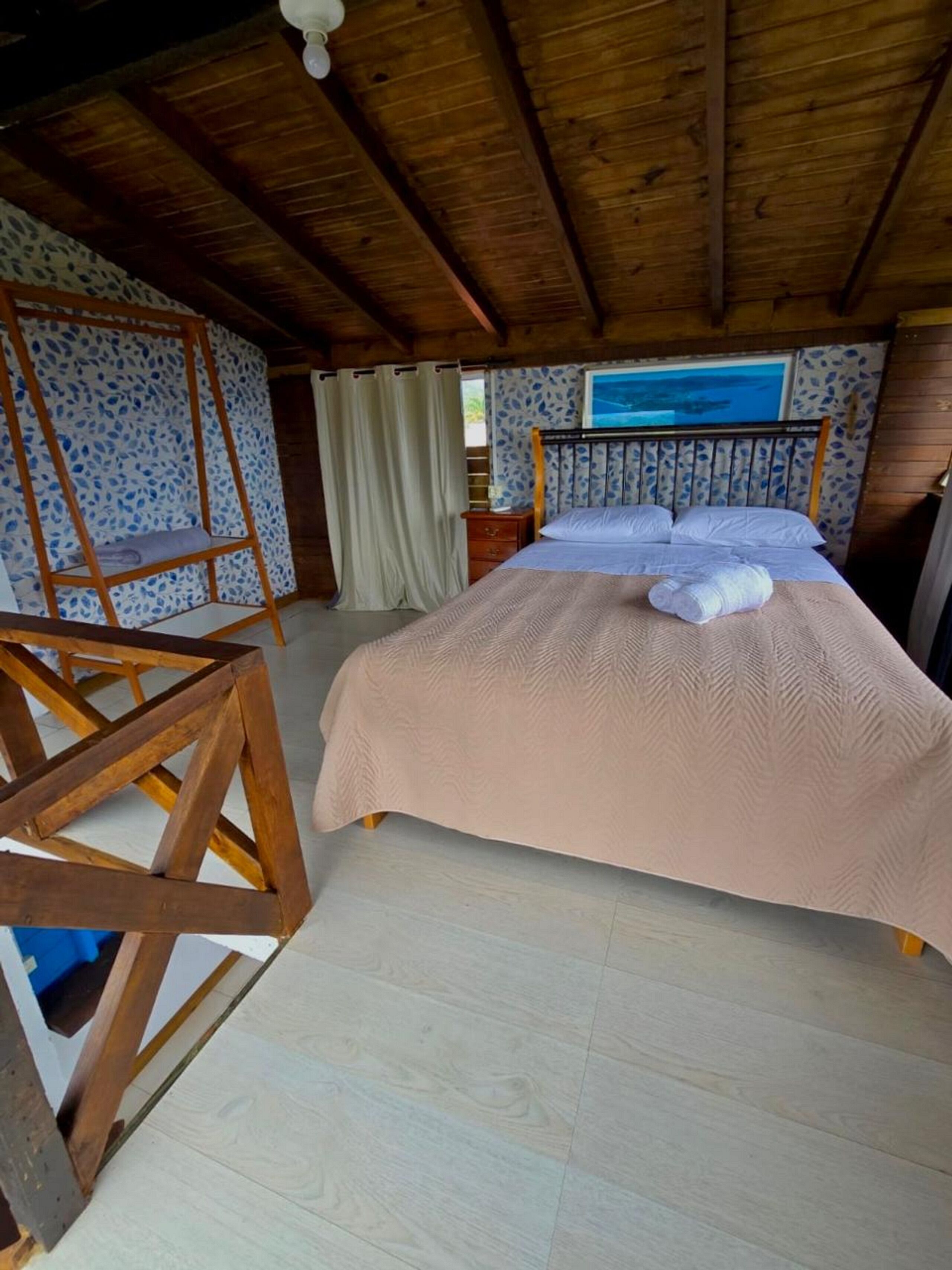 Un dormitorio con cama, techo de madera, cortinas estampadas y vistas al exterior.