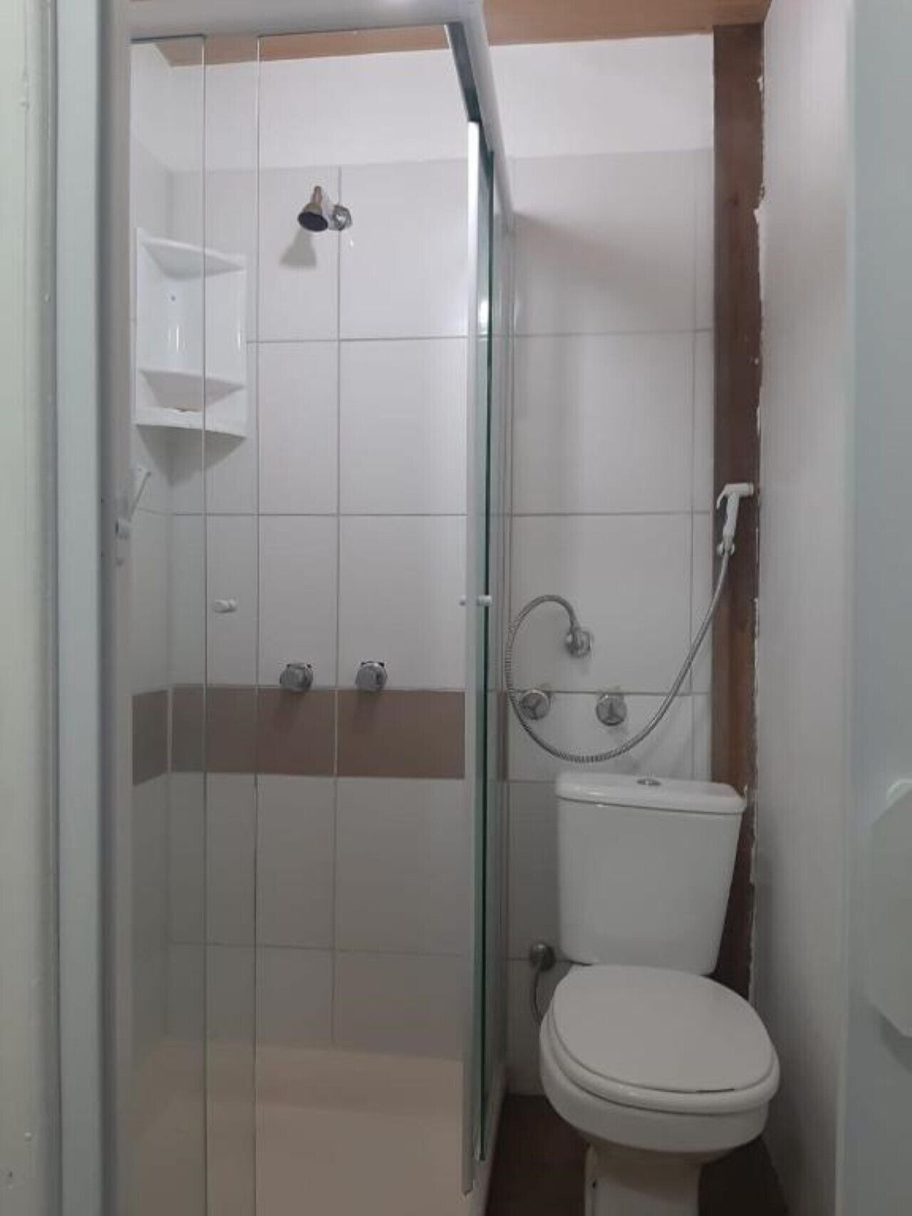 Une petite salle de bain avec une douche à parois de verre, des toilettes et une étagère au-dessus des toilettes.