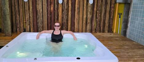 A person relaxing in a wooden deck hot tub with a wooden fence backdrop.