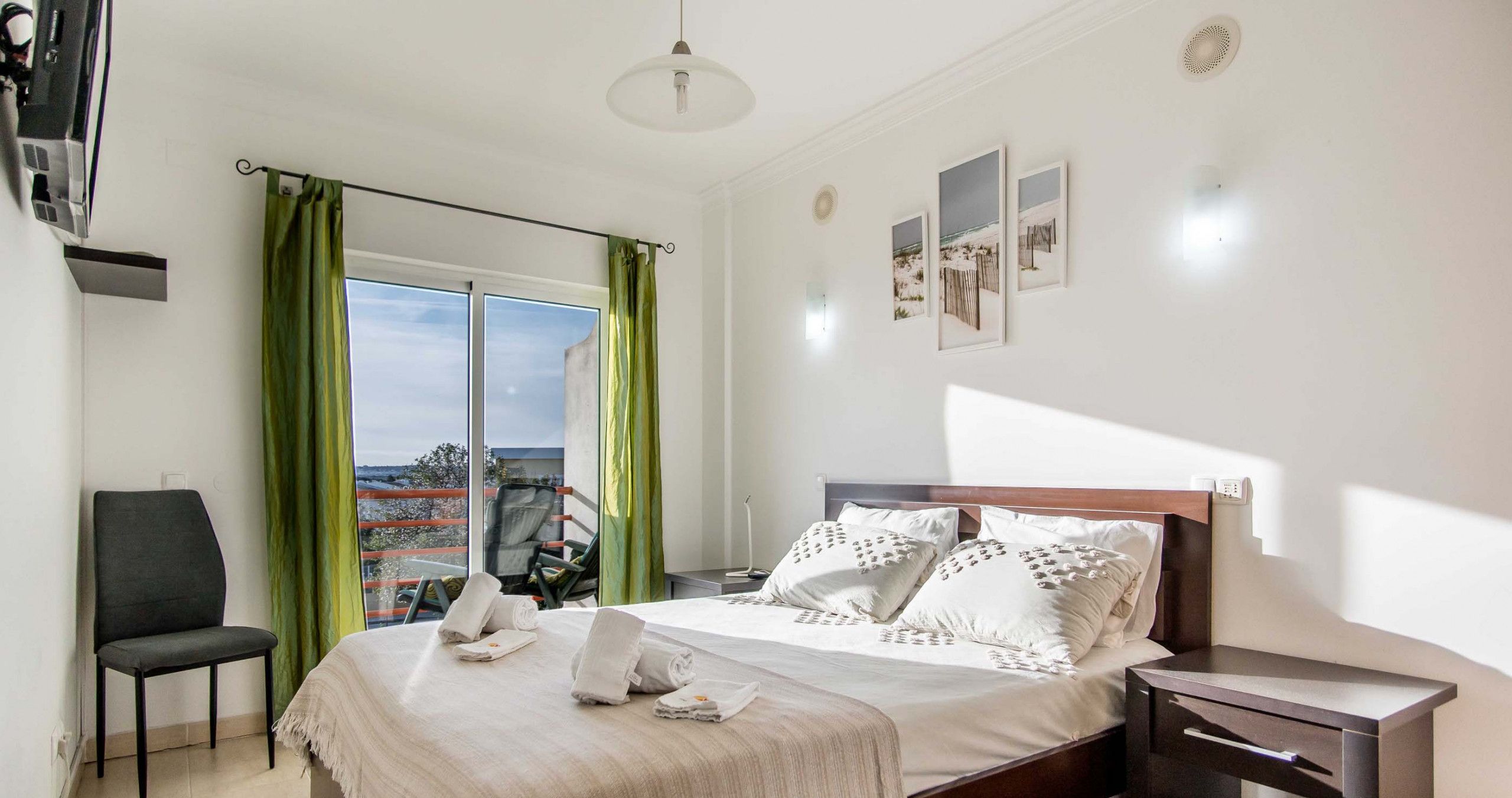 Quarto com cama, uma cadeira, mesa de cabeceira e vista para o exterior.