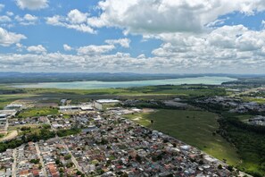 An aerial view of a town with residential areas, industrial buildings, and a large body of water in the background. - Samba Linhares (Linhares)