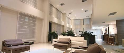 A spacious living area with modern furniture, large windows, and a high ceiling.
