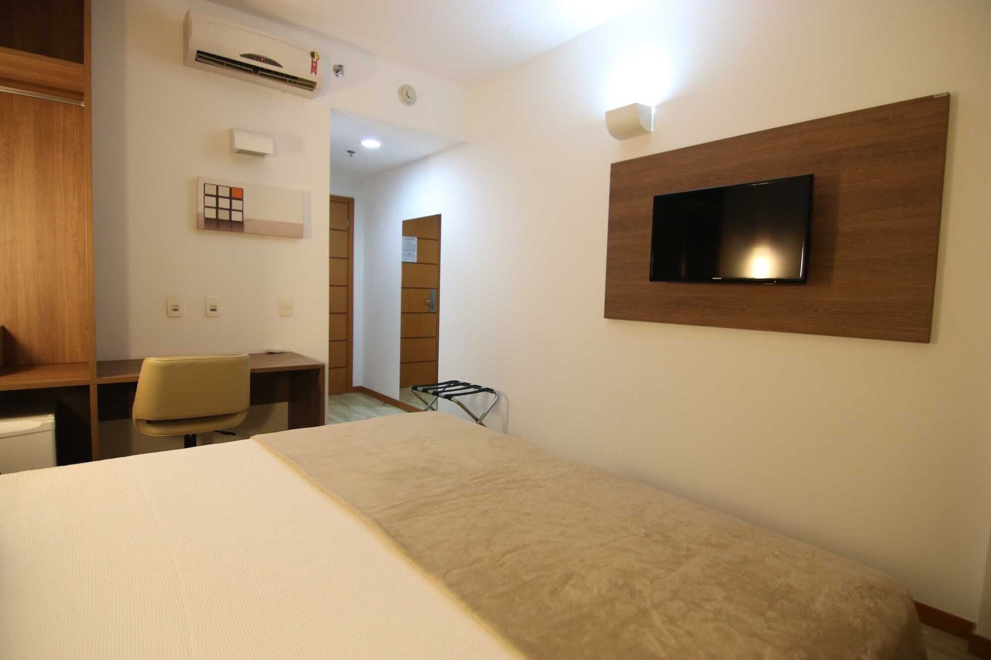 Habitación de hotel con cama, escritorio, silla, televisor montado en la pared y aire acondicionado.