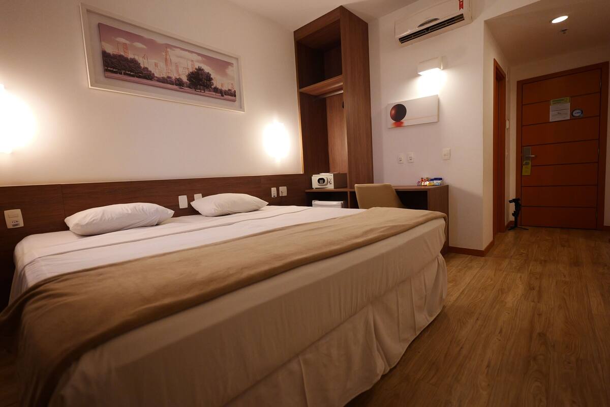 Habitación de hotel con una cama grande, un escritorio, una silla y un armario de madera.