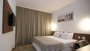 Habitación de hotel con una cama, un televisor de pantalla plana montado en la pared, un cuadro sobre la cama y un escritorio con una silla.