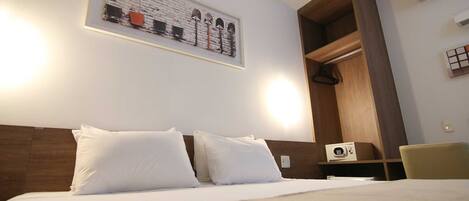 A hotel room with a bed, a wooden headboard, a wall-mounted artwork, a coat rack, and a small table with a radio.