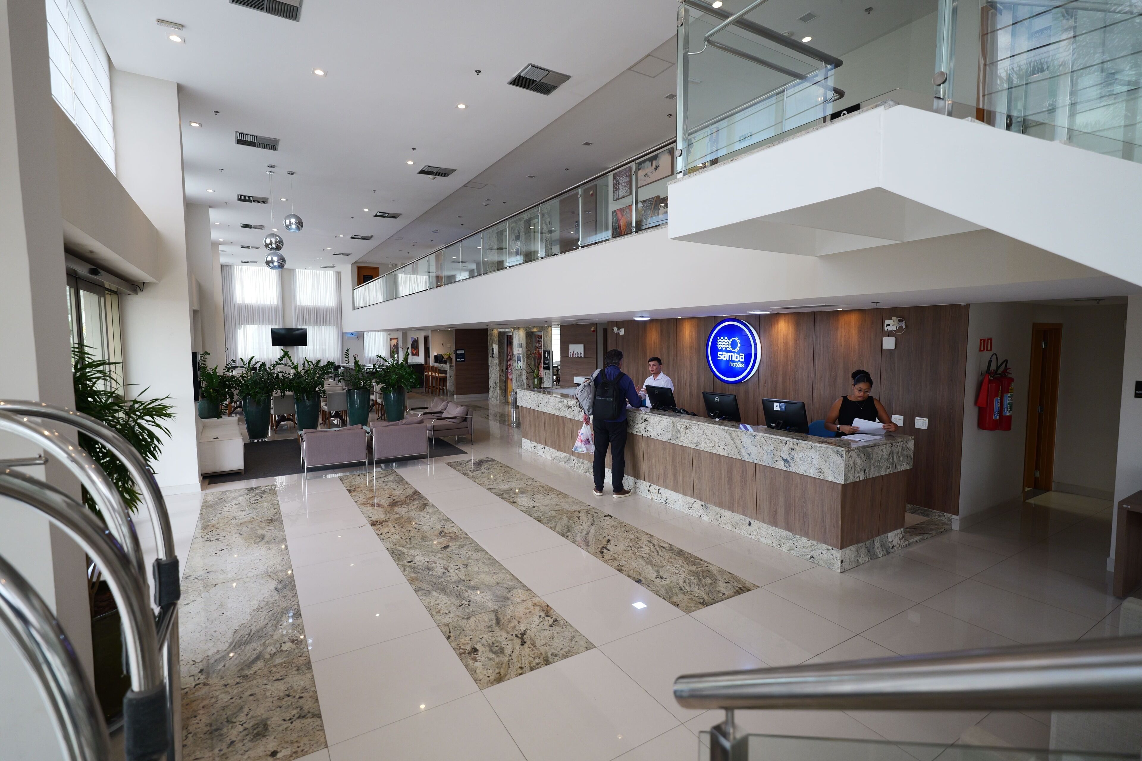 A modern hotel lobby with a reception desk, seating area, and a glass railing on the upper level.