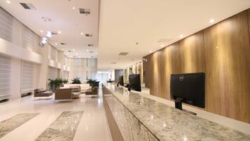 Un moderno hall de hotel con un mostrador de recepción alargado, una zona de estar confortable y grandes ventanales.