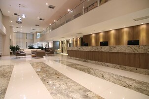 Um hall amplo com piso de mármore, balcão de recepção com acabamento em madeira e área de estar com sofás.