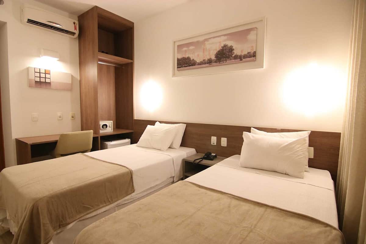 Habitación de hotel con dos camas, un escritorio, una silla, un cuadro en la pared y un armario empotrado.