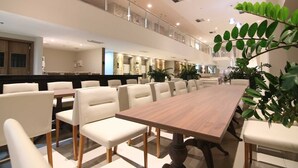 Un comedor amplio con una larga mesa de madera y sillas blancas tapizadas, rodeado de plantas en macetas.