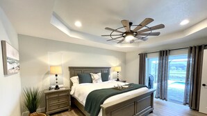 Une chambre à coucher avec un lit, des lampes de chevet, un ventilateur de plafond, une fenêtre avec des rideaux et une vue sur l’extérieur.