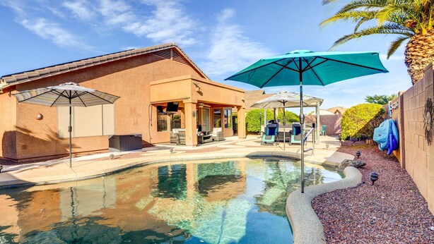 A swimming pool with a patio area, umbrellas, and a brick building.