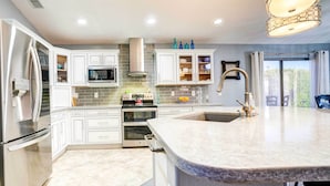 A modern kitchen with white cabinetry, stainless steel appliances, a large island, and a view to the outside.